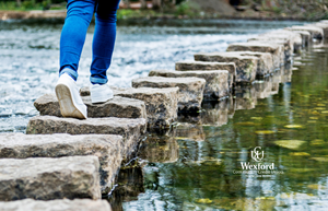 Person walking across a stepping-stone bridge over water.